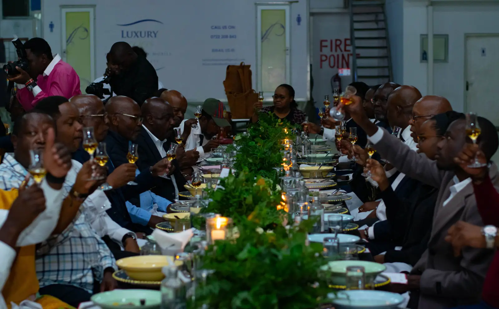 Guests raising glasses in a toast during a luxury corporate dinner event planned by Kokoro Group, set at an elegant long table with candlelit greenery.